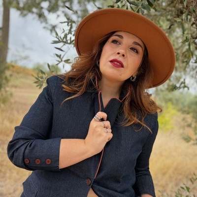 Mulher com blazer azul escuro e chapéu castanho ao ar livre