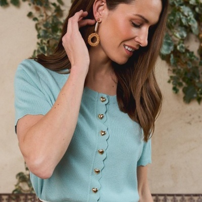 Mulher com camisola azul clara com botões dourados em forma de coração e cinto castanho