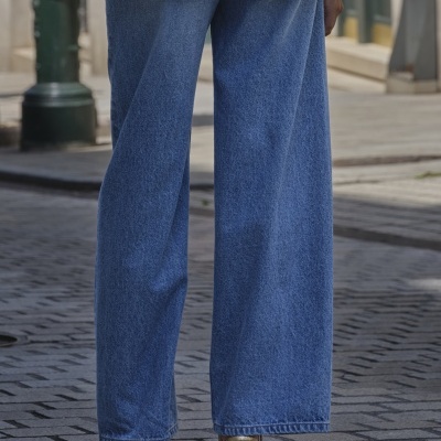 Calças de ganga largas azuis com sapatos dourados de salto alto em calçada