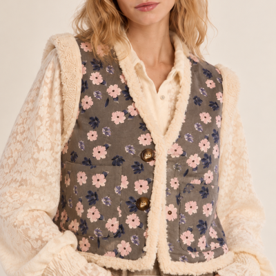 Colete floral com guarnição felpuda em mulher vestindo camisa de renda e calças bege