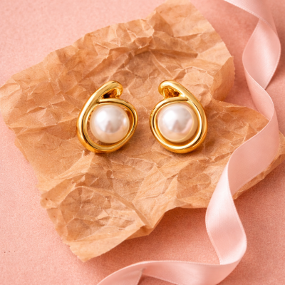 Brincos dourados com pérolas sobre papel pardo e fita de cetim cor-de-rosa