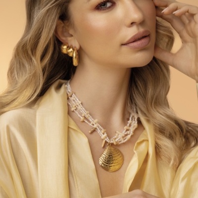 Colar e brincos dourados usados por mulher com camisa amarela clara