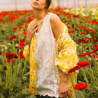 Mulher com blusa branca bordada e casaco amarelo floral em campo de flores vermelhas