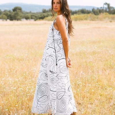 Mulher com vestido comprido branco com padrão abstrato preto num campo de relva seca