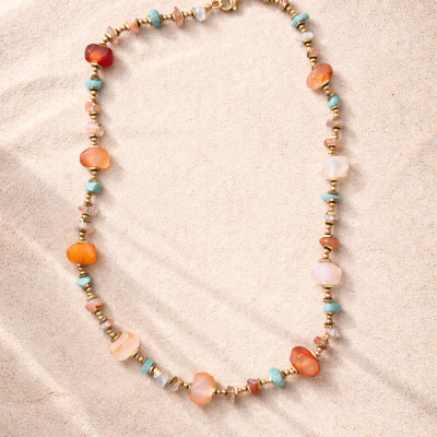 Colar colorido com pedras e contas douradas sobre areia clara