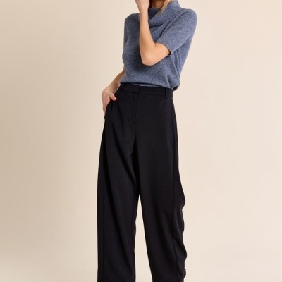Mulher com camisola azul de malha e calças largas pretas.