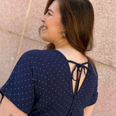 Pessoa com vestido azul escuro com pequenos pontos brancos e laço nas costas frente a parede cor de rosa.
