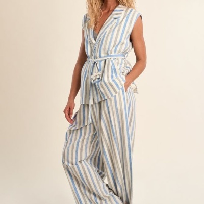 Mulher vestindo conjunto riscado azul e branco com colete e calças largas em fundo neutro