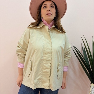 Mulher com casaco bege, camisa riscada rosa e branca, calças de ganga azul e chapéu rosa claro em fundo rosa