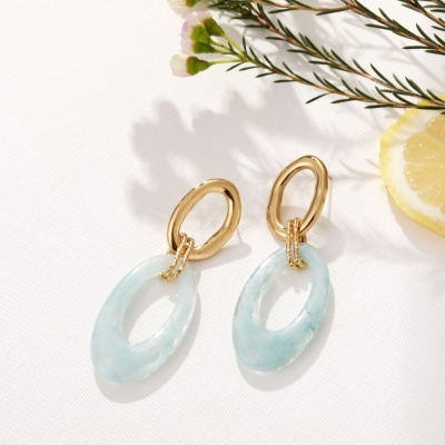 Brincos dourados e azul celeste marmoreado com limão e flores ao lado