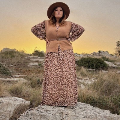 Mulher com vestido animal print e colete castanho com cinto, chapéu castanho, ao ar livre em área rochosa