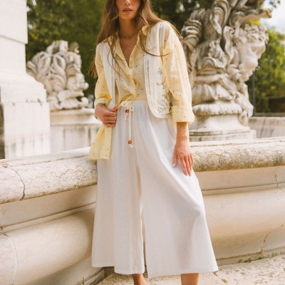 Mulher com roupa clara e sapatos castanhos junto a esculturas de pedra