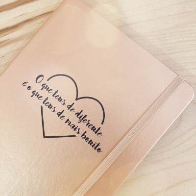 Caderno de capa dura rosa com texto em preto e elástico lateral