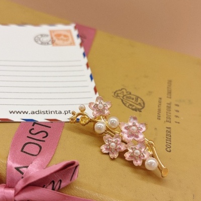 Broche flores rosa e pérolas sobre caixa amarela com fita rosa e texto