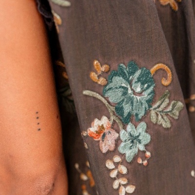 Tecido castanho com bordados florais coloridos e braço com tatuagem de quatro pontos