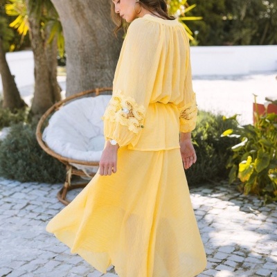 Vestido amarelo com renda e pérolas, mulher em jardim com cadeira de vime.