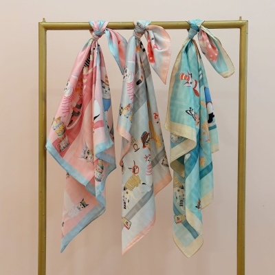 Três lenços coloridos com padrão de gatos pendurados num cabide dourado