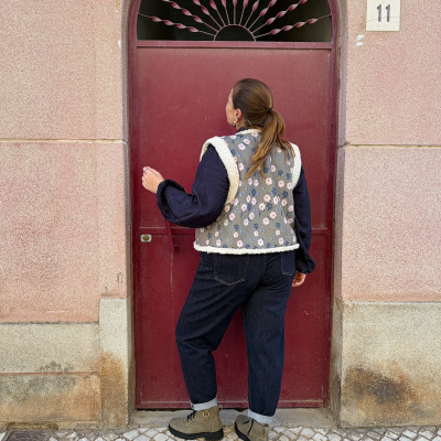 Pessoa de costas com colete floral em frente a porta vermelha arquada com número 11 na parede rosa