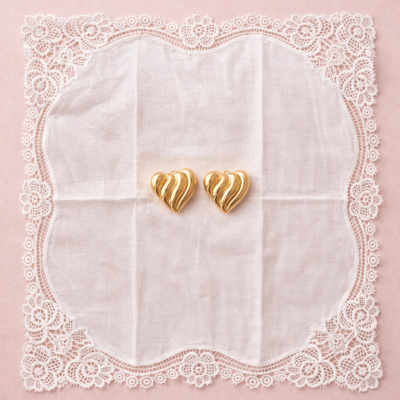 Brincos dourados em forma de coração sobre lenço branco com renda cole floral