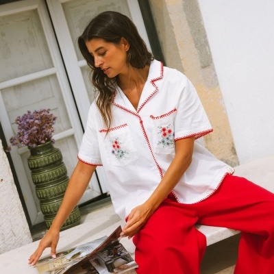 Camisa branca bordada com detalhes vermelhos e calças vermelhas largas, em ambiente exterior