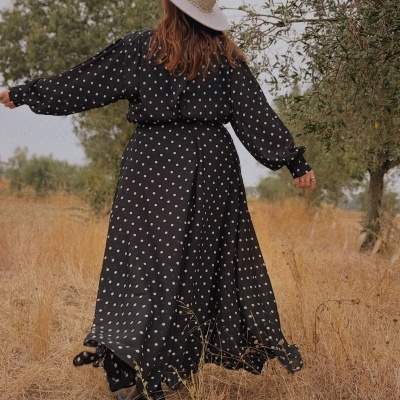 Vestido comprido preto de bolinhas com chapéu bege num campo seco