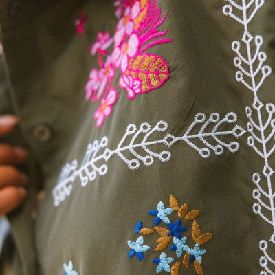 Pormenor de tecido verde com bordados florais coloridos e botão castanho