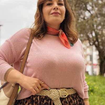 Mulher com camisola rosa, cinto dourado e saia animal print ao ar livre