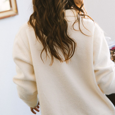 Camisola creme de malha vista de costas com cabelo castanho ondulado