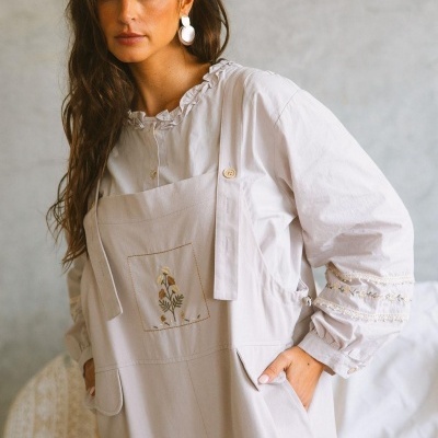 Macacão bege claro com padrão floral bordado e camisa branca com folhos e bordados nas mangas