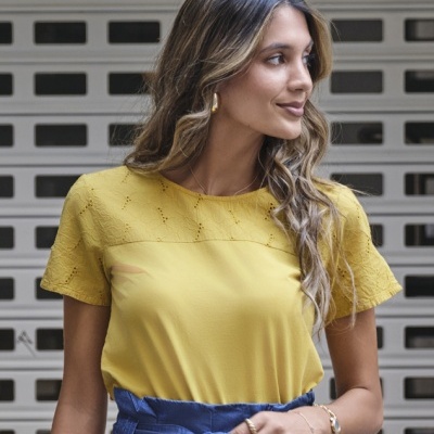 Mulher com blusa amarela rendada e saia/calça azul com cinto
