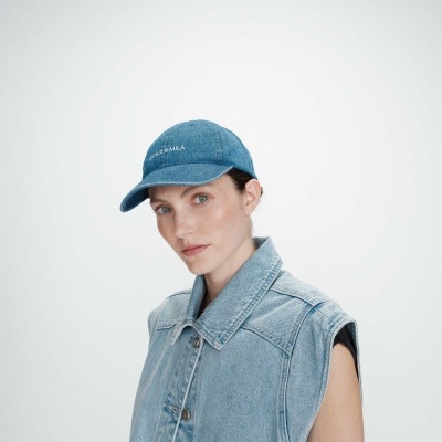 Mulher com boné azul de ganga e colete de ganga azul claro sem mangas.