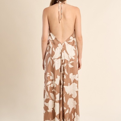 Mulher vista de costas a usar vestido comprido castanho com flores brancas e sandálias de salto grosso.