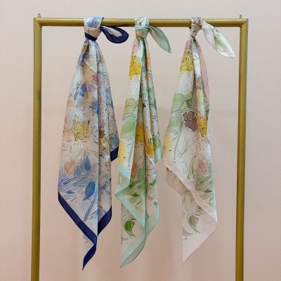 Três lenços florais em tons pastel pendurados num cabide dourado