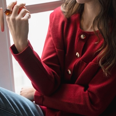 Casaco de malha vermelho com botões dourados e calças de ganga azul claro perto de janela