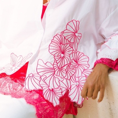 Blusa branca com bordado floral rosa e detalhes de pérolas, com renda rosa por baixo.