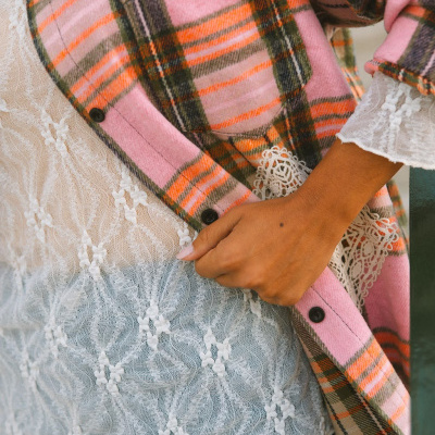 Camisa xadrez rosa, laranja e verde com blusa branca rendada e mão à cintura