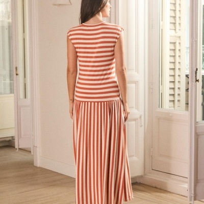 Vestido longo riscado branco e laranja visto de costas em ambiente interior com chão de madeira