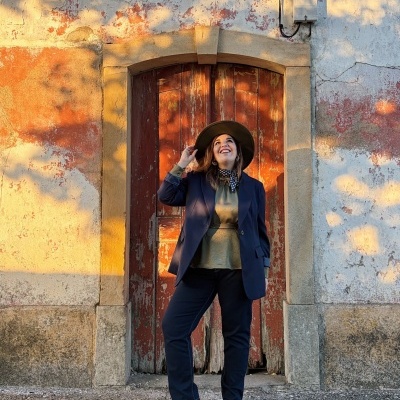Mulher com roupa formal azul e chapéu castanho em porta vermelha antiga com parede desgastada
