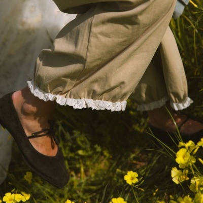 Calças bege com renda branca na bainha e sapatos pretos em relva com flores amarelas