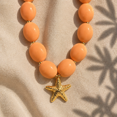 Colar com contas cor de coral e pendente estrela-do-mar dourado sobre tecido bege.