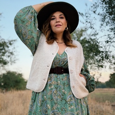 Vestido verde com padrão paisley e colete branco felpudo com chapéu preto ao ar livre