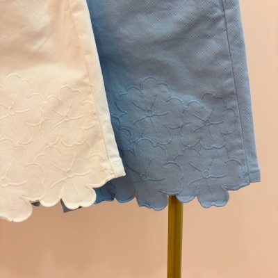 Bainhas de tecido creme e azul com bordado floral e recorte em cima de suporte amarelo.