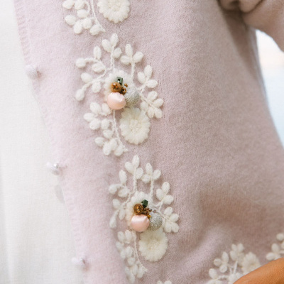 Casaco rosa claro com padrão floral branco e flores decorativas em tricô