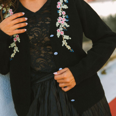 Cardigan preto com bordados florais e botões usados com blusa renda e saia preta.