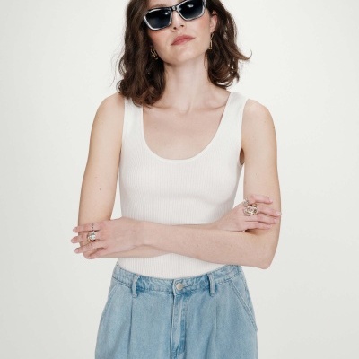 Mulher com top branco e calças de ganga azuis com óculos de sol negros