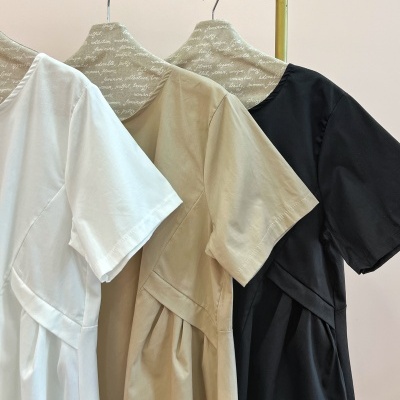 Vestidos branco, bege e preto pendurados em cabides com tecido impresso em texto branco, em cabide dourado