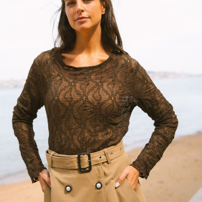 Camisola rendada castanha com saia bege de cintura alta junto ao mar.