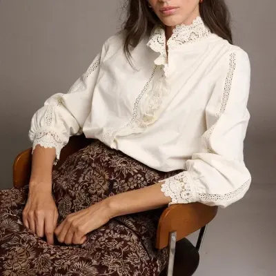 Mulher sentada numa cadeira, blusa creme com renda e saia castanha com padrão floral
