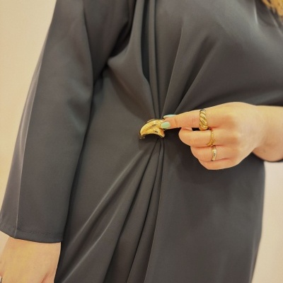 Vestido cinza com prega e fivela dourada e mão feminina com anéis