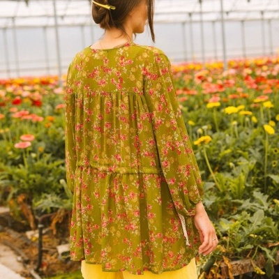 Vestido verde floral com mangas compridas visto de costas em estufa de flores coloridas